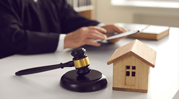 Judge with gavel and wooden house model on desk, symbolizing legal aspects of property sales and cash offers for distressed homeowners.
